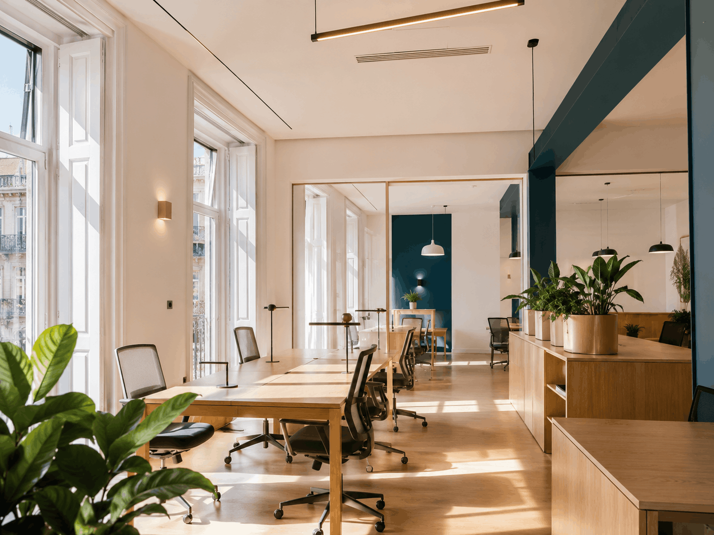 Mesas de coworking com luz natural, cadeiras ergonómicas e detalhes em verde profundo